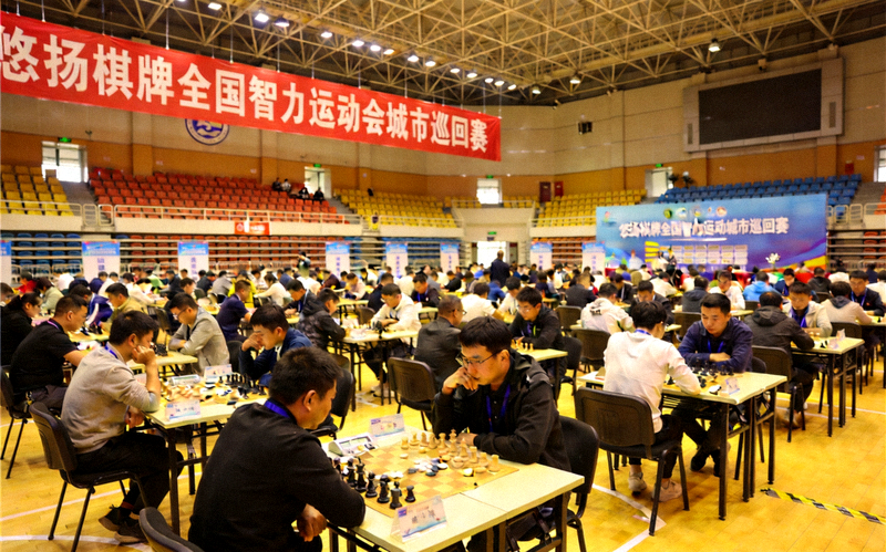 悠扬棋牌全国智力运动会城市巡回赛现场，棋手在整齐的棋桌前专注对弈
